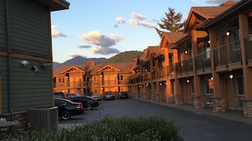 A row of multi-story buildings with balconies, a parking area, and a mountain in the background.