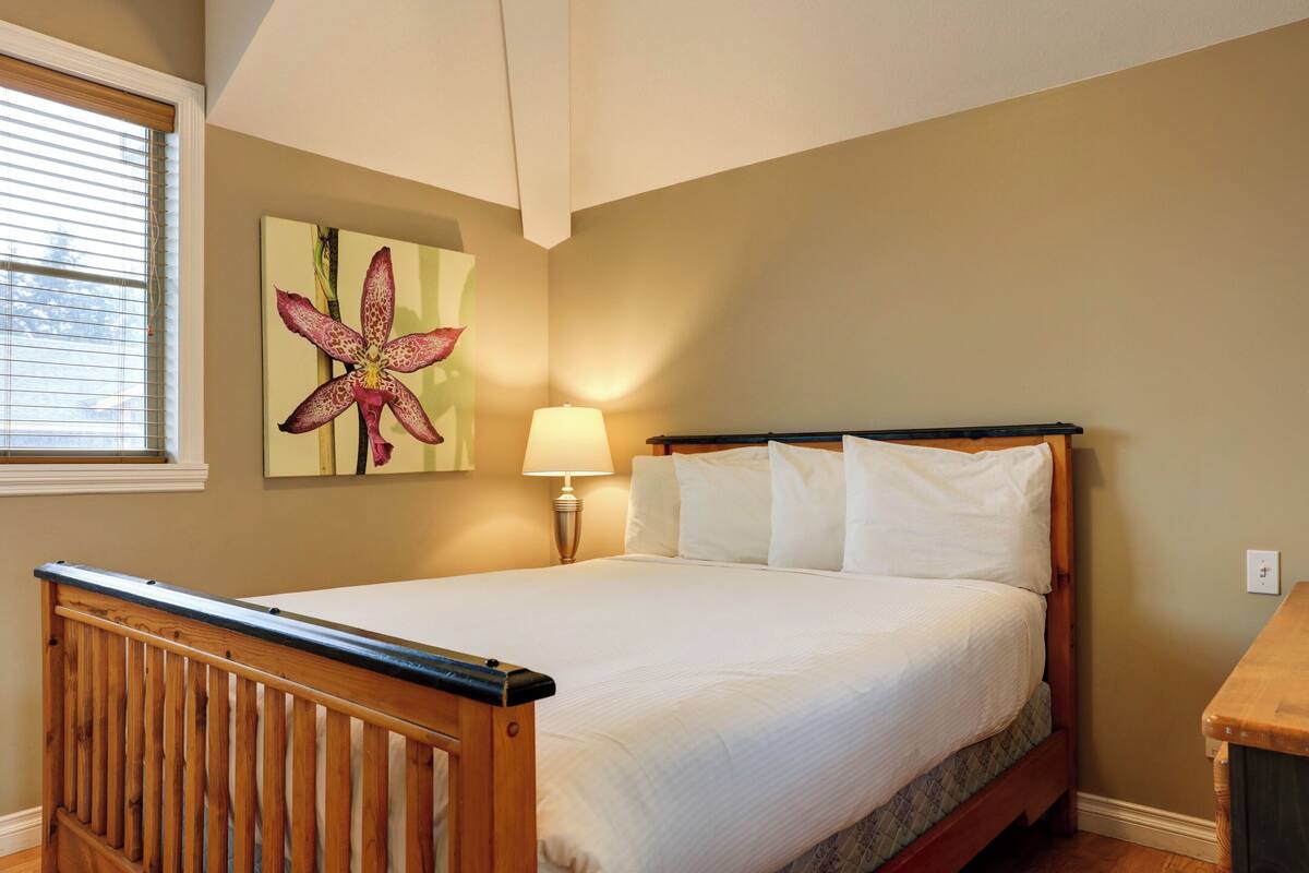 A bedroom with a wooden bed, a nightstand, a lamp, and a large flower painting on the wall.