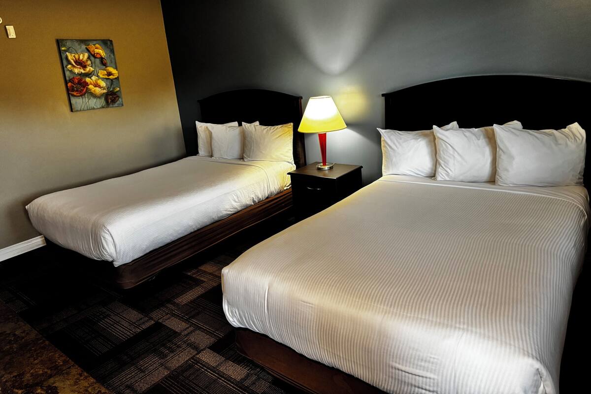 A hotel room with two beds, a nightstand with a lamp, and a painting on the wall.