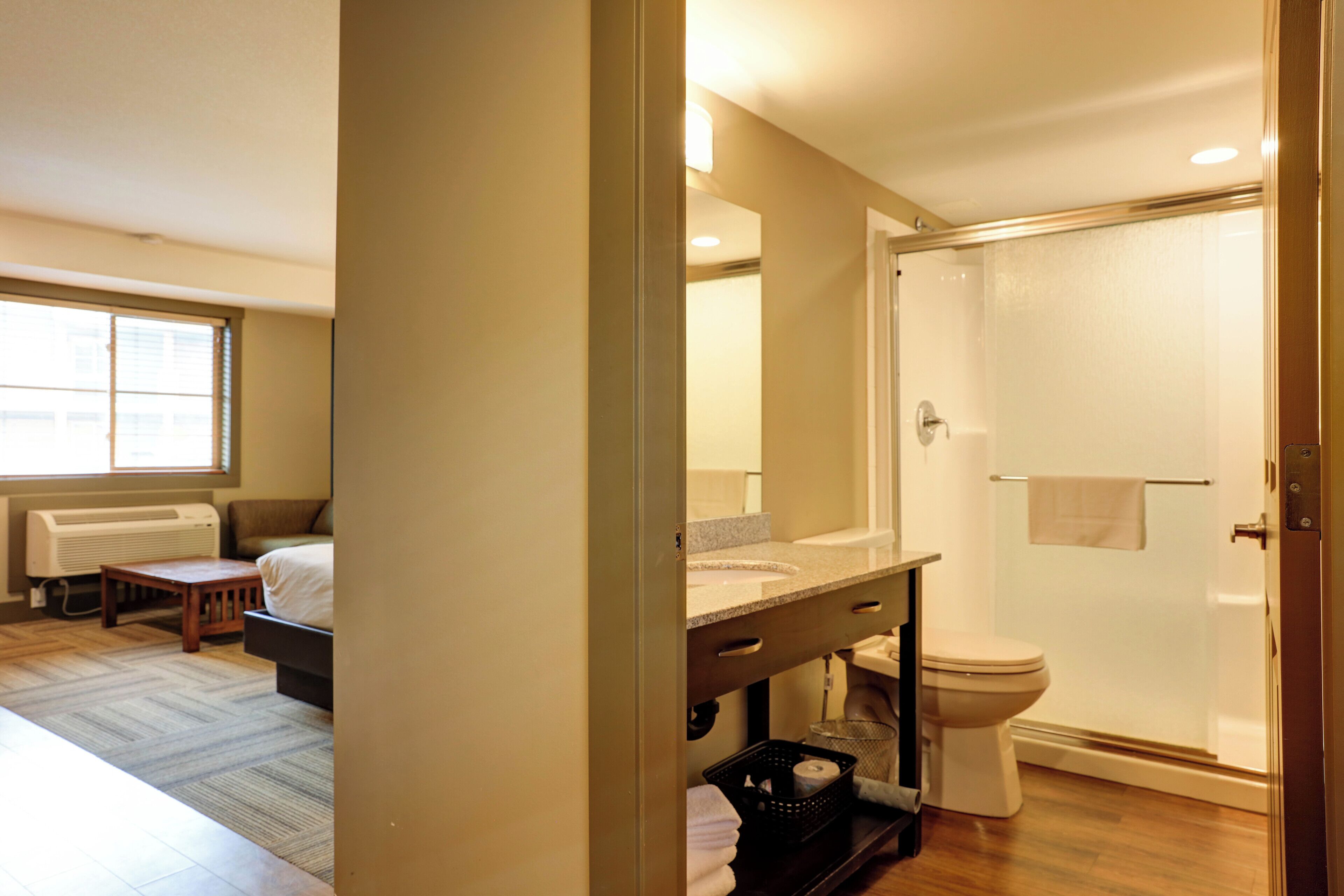 A bathroom with a shower, toilet, sink, and a small table.