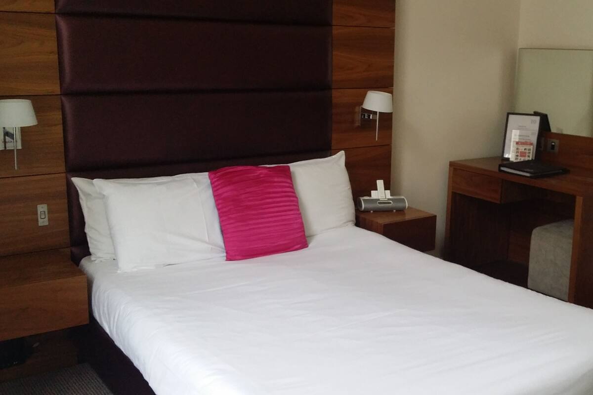 A hotel room with a large bed, a wooden headboard, a desk with a chair, a lamp, and a telephone.