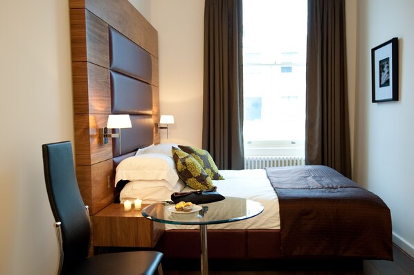 A hotel room with a bed, a small table with a plate of food, a chair, and a lamp. - 10 Pembridge Gardens (London)