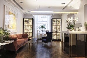 A modern living room with a brown sofa, a dark blue armchair, a glass coffee table, and a bookshelf filled with decorative items.