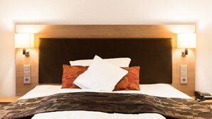A hotel room with a wooden headboard, two bedside lamps, a telephone, and a bed with white and patterned bedding.