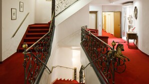 A grand staircase with ornate metal railings and red carpeted steps leading to an upper floor.