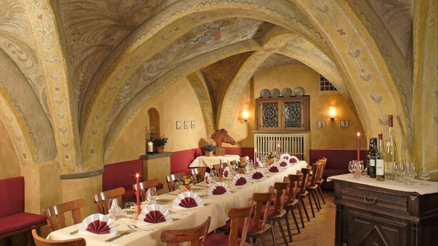 A long dining table set for a meal in a room with high, vaulted ceilings and ornate wall decorations.