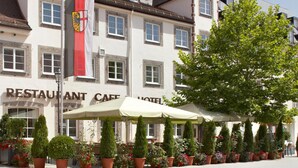 A building with a sign reading "RESTAURANT CAFE HOTEL". There are outdoor umbrellas and potted plants in front.