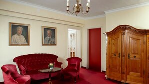 A room with a red velvet sofa, two red armchairs, a wooden cabinet, and two framed portraits on the wall.