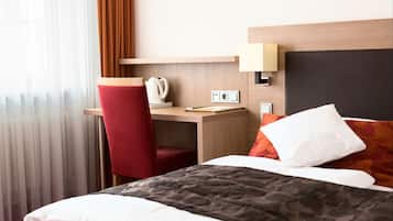 Una habitación de hotel con una cama, un escritorio con una silla, una lámpara y un ventanal con cortinas.