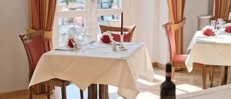 Comedor con mesas dispuestas para dos, con manteles blancos y servilletas rojas.
