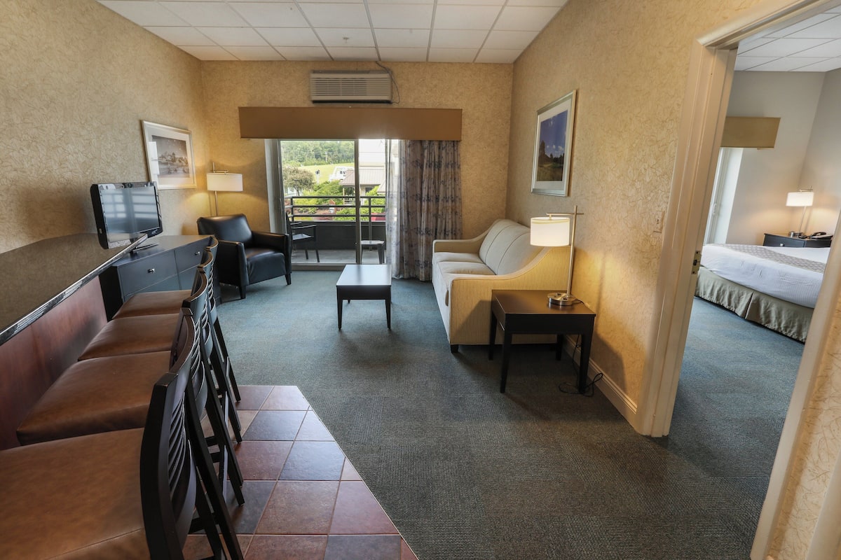 A hotel room with a seating area, a bed, a desk, and a view of the outdoors.