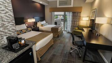 A hotel room with two beds, a desk with a coffee maker, a chair, and a view of the outdoors.