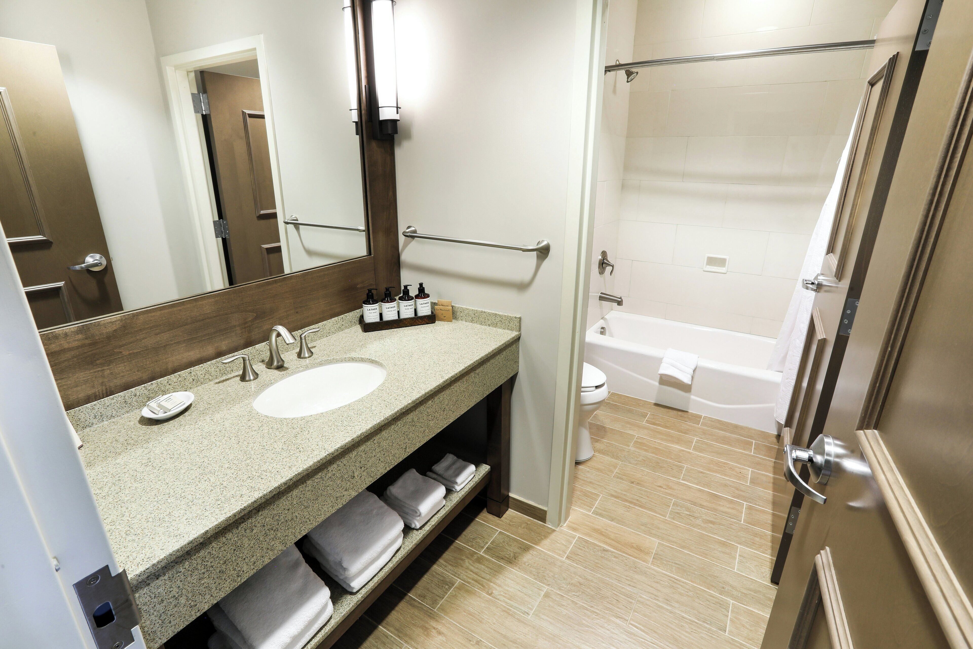 A modern bathroom with a granite countertop, two sinks, a large mirror, and a walk-in shower.