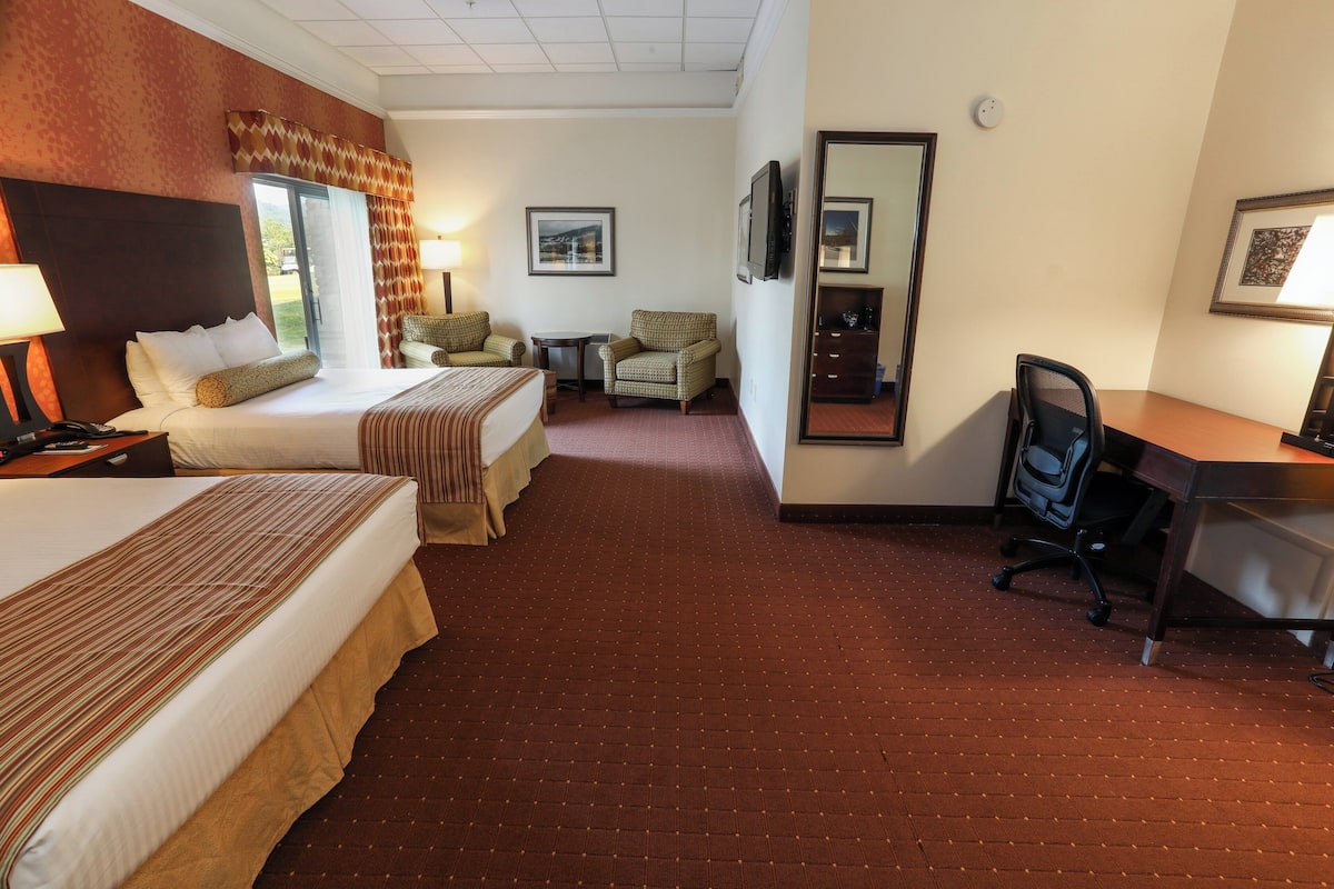 A hotel room with two beds, a desk, a chair, a TV, and a mirror.