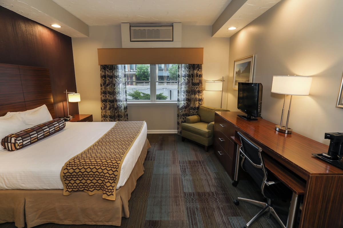 A hotel room with a large bed, a desk with a chair, a television, and a window with curtains.