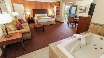 A hotel room with a bed, a sofa, a desk, a chair, a TV, and a bathtub.