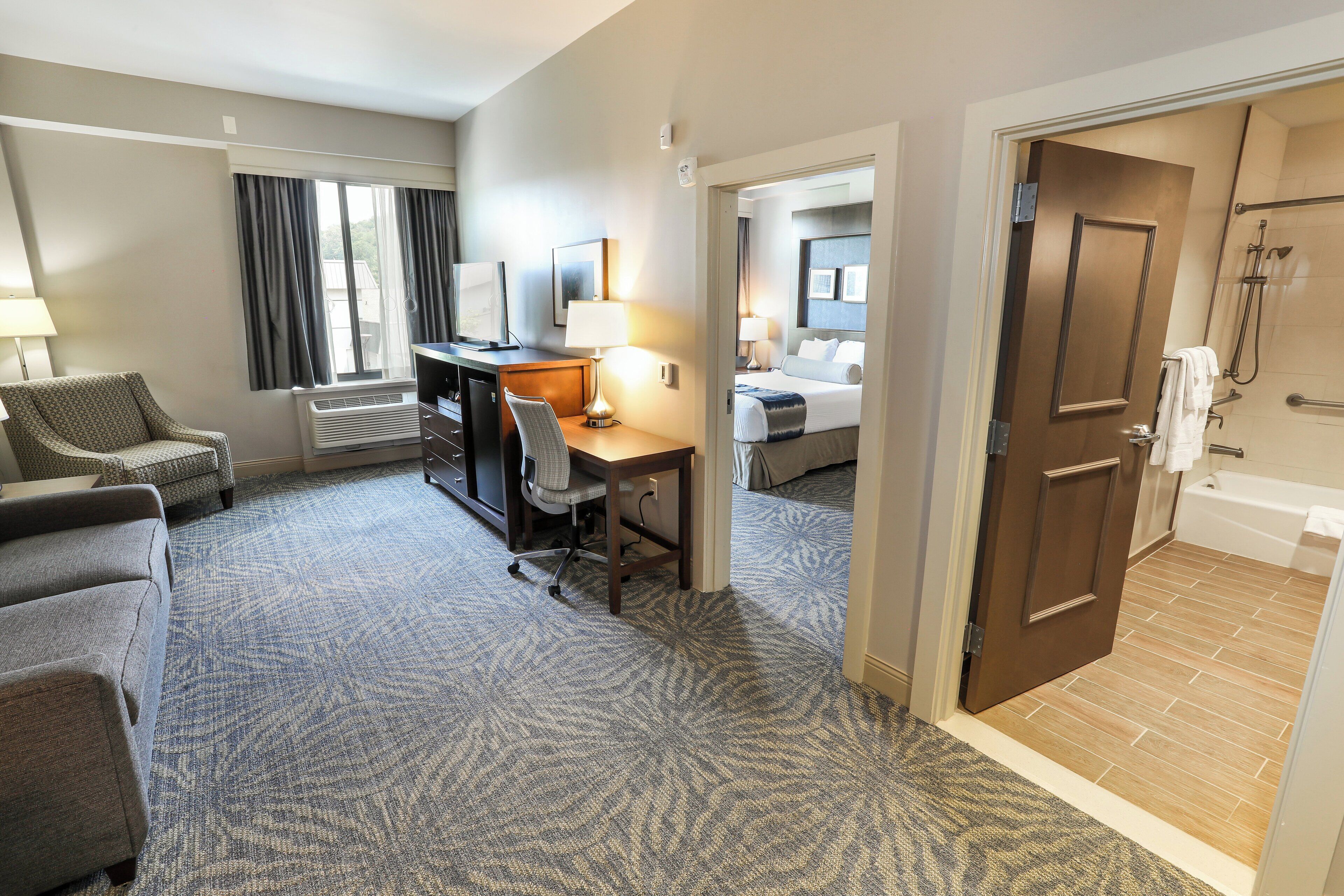 A hotel room with a desk, chair, and a bed. There is a bathroom with a bathtub and a shower.