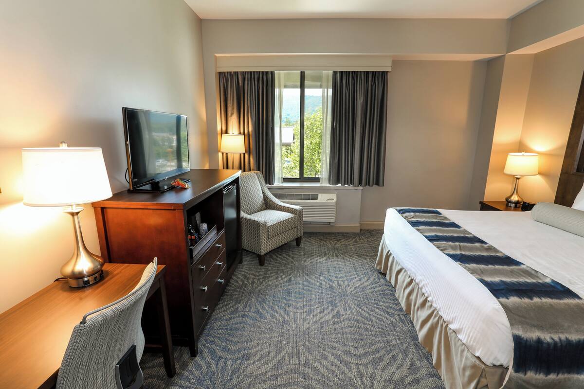 A hotel room with a bed, desk, chair, television, and two lamps.