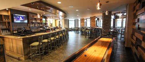 A bar area with a pool table, bar stools, and a television screen.