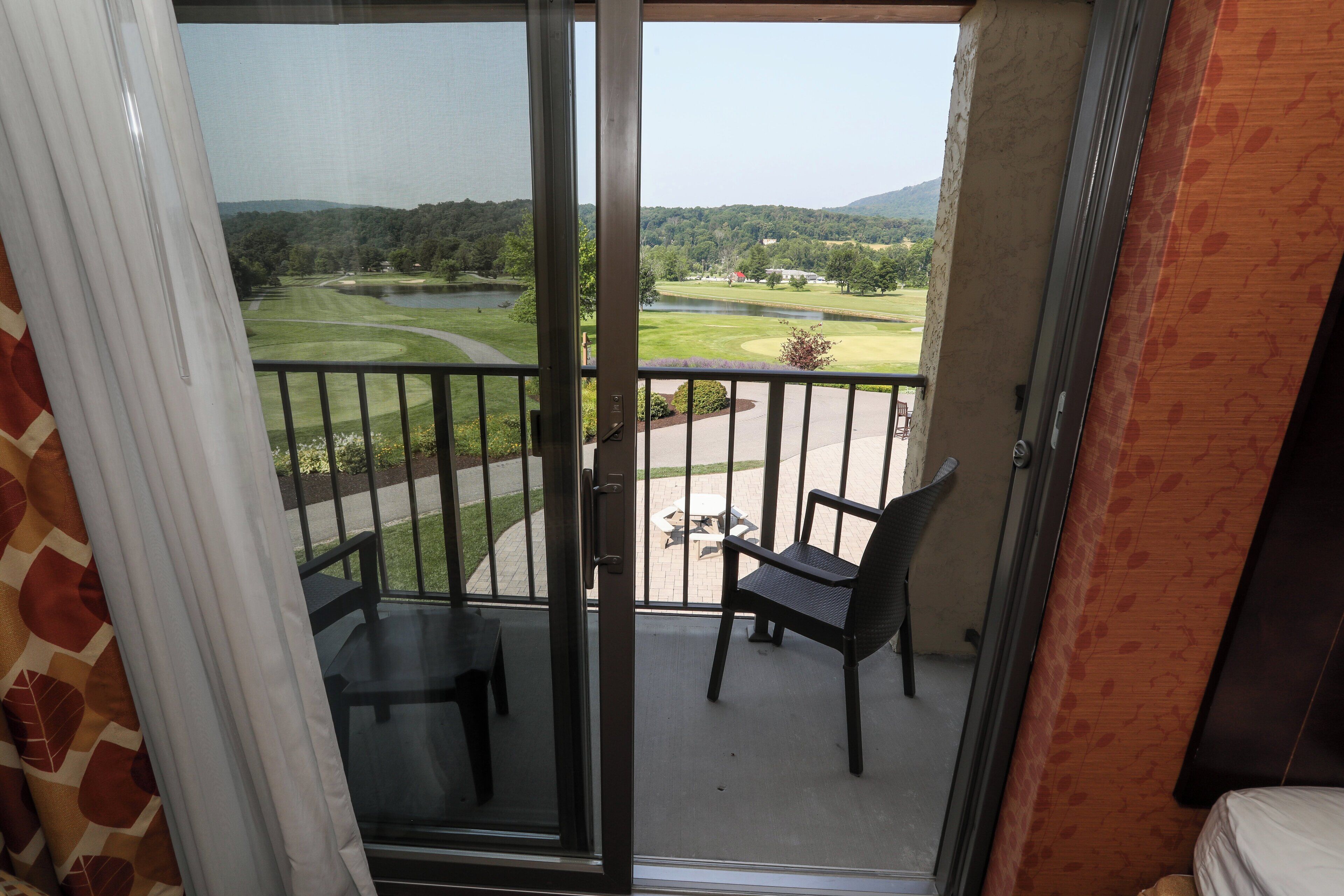 Un balcon avec vue sur un terrain de golf et un lac. On y trouve deux chaises et une table.