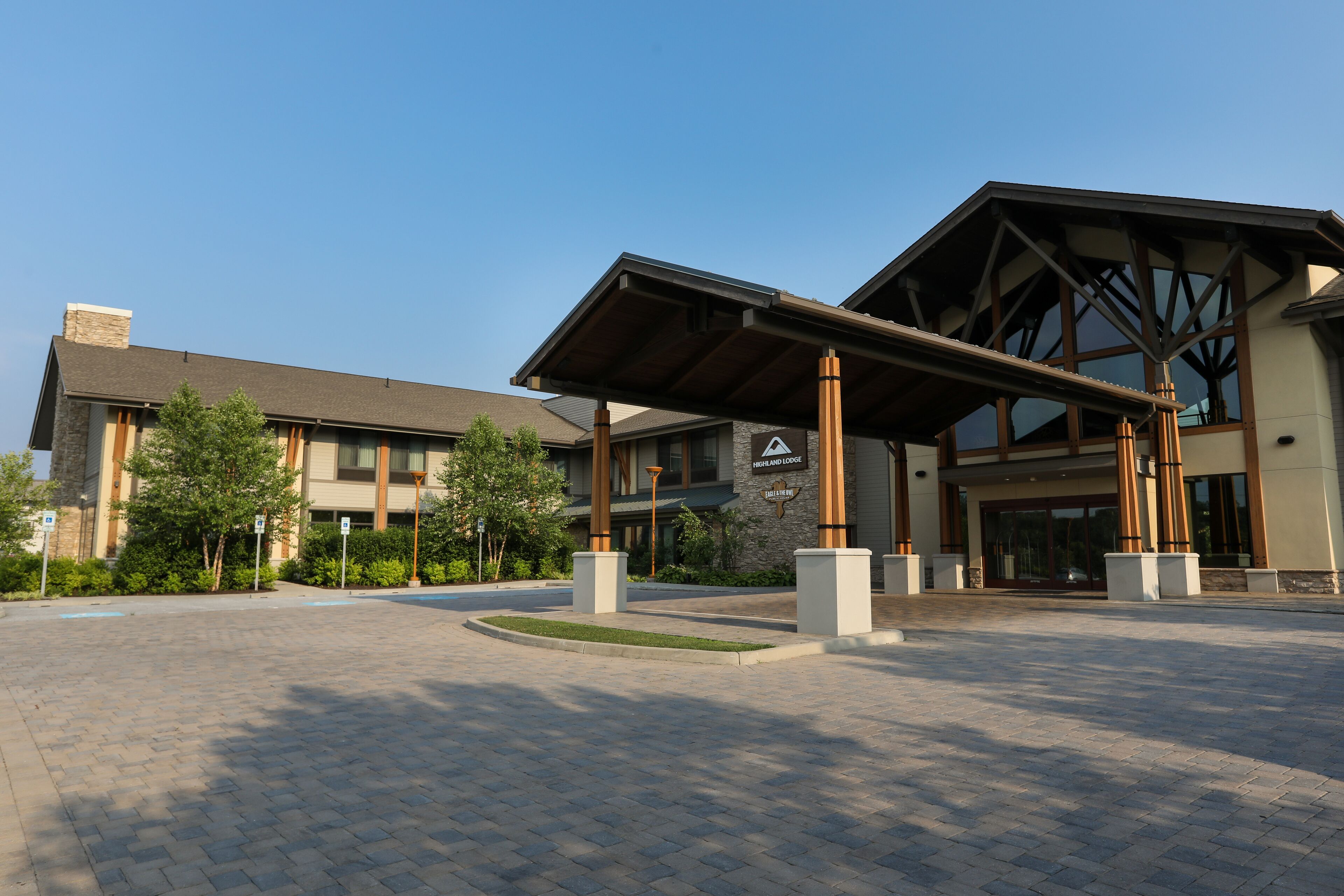 A building with a covered entrance, stone pillars, and a landscaped area with trees.