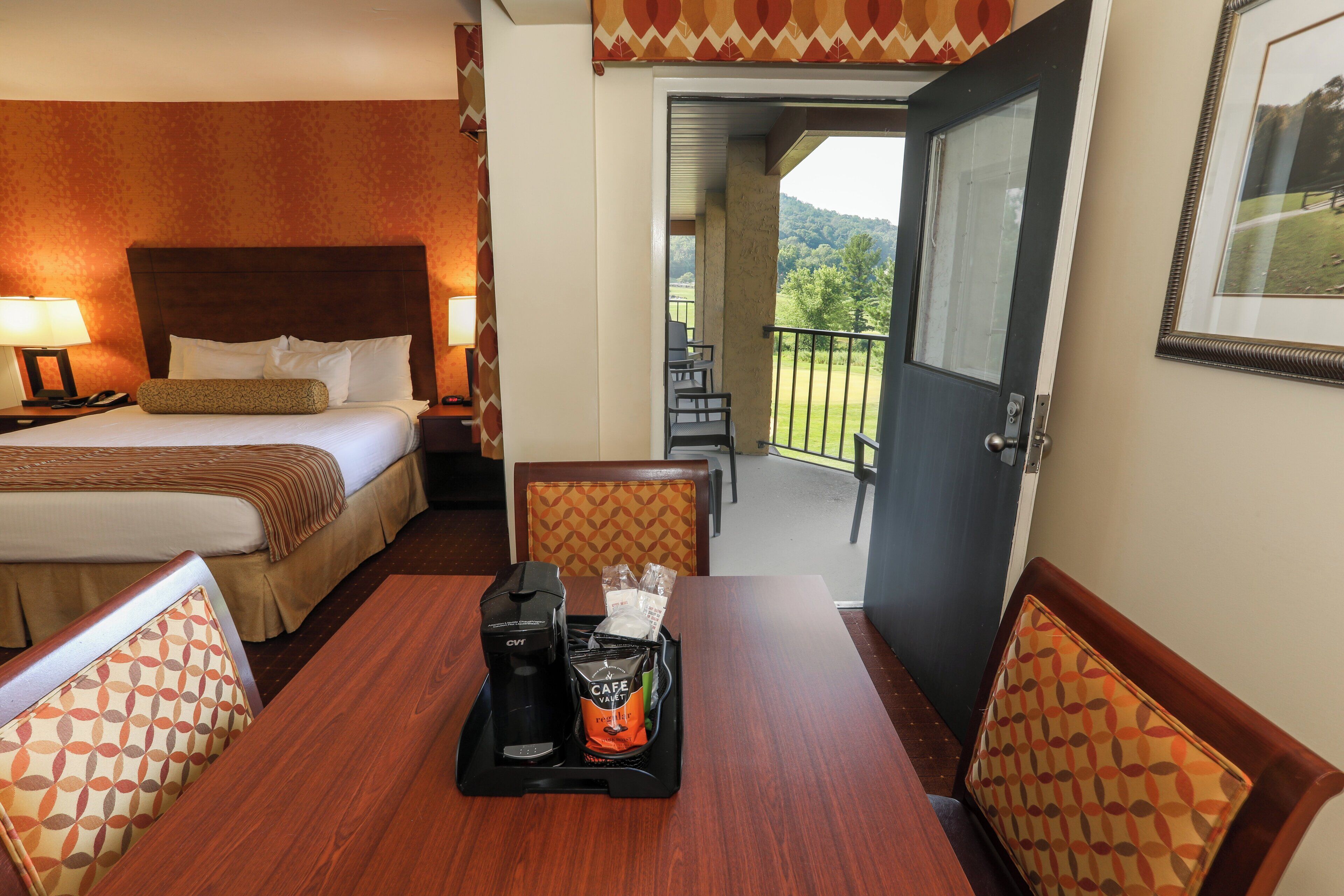 A hotel room with a bed, bedside table, lamp, and a dining area with a tray of coffee and breakfast items.