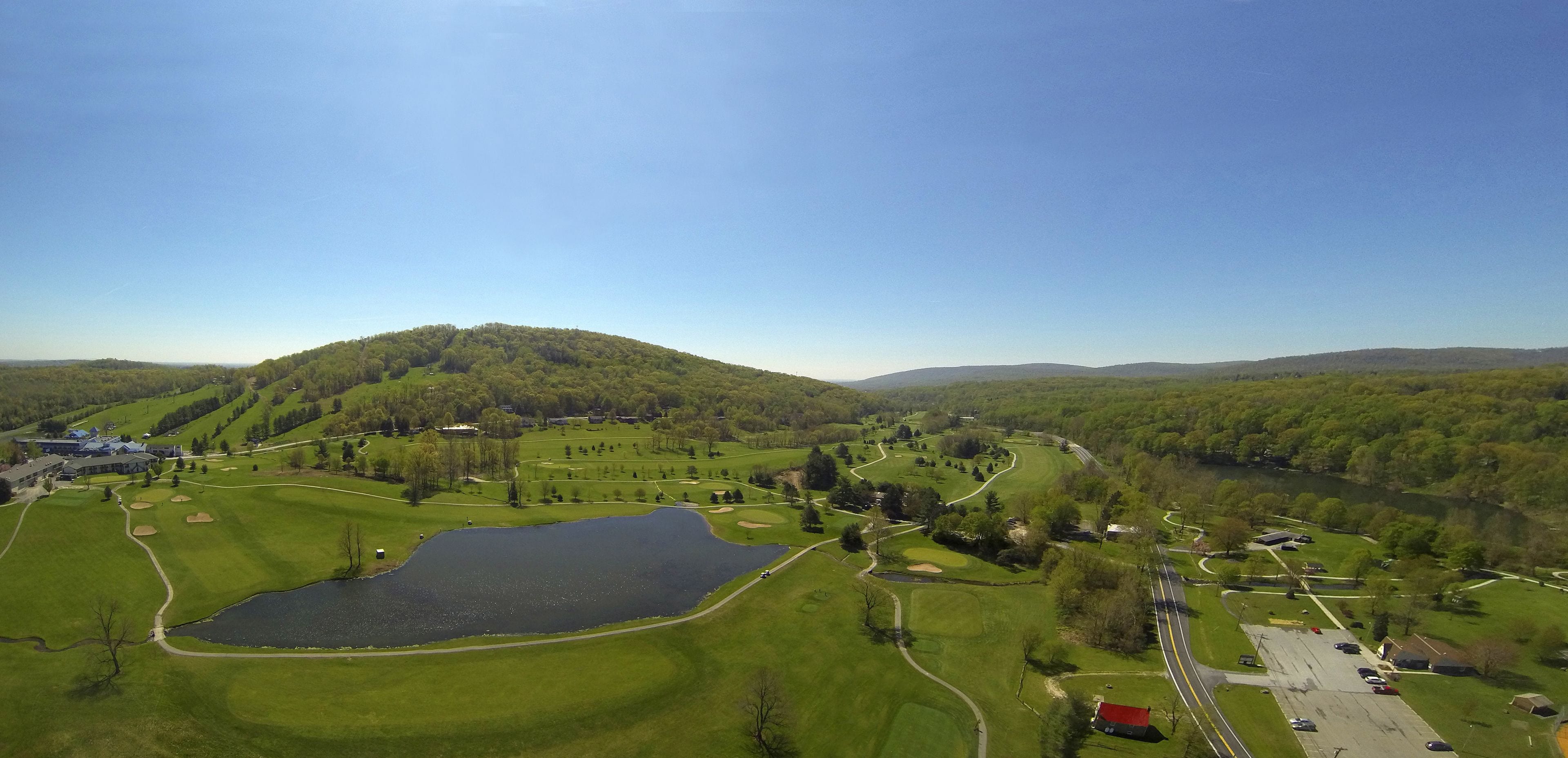 Un campo da golf con uno stagno, una club house e un'area di parcheggio.