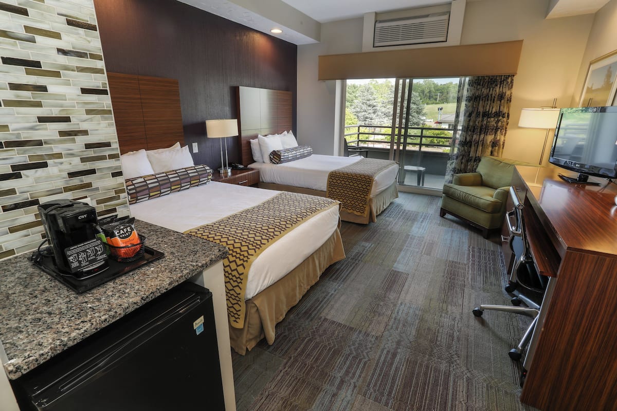 A hotel room with two beds, a desk with a TV, a coffee maker, and a view of the outdoors.