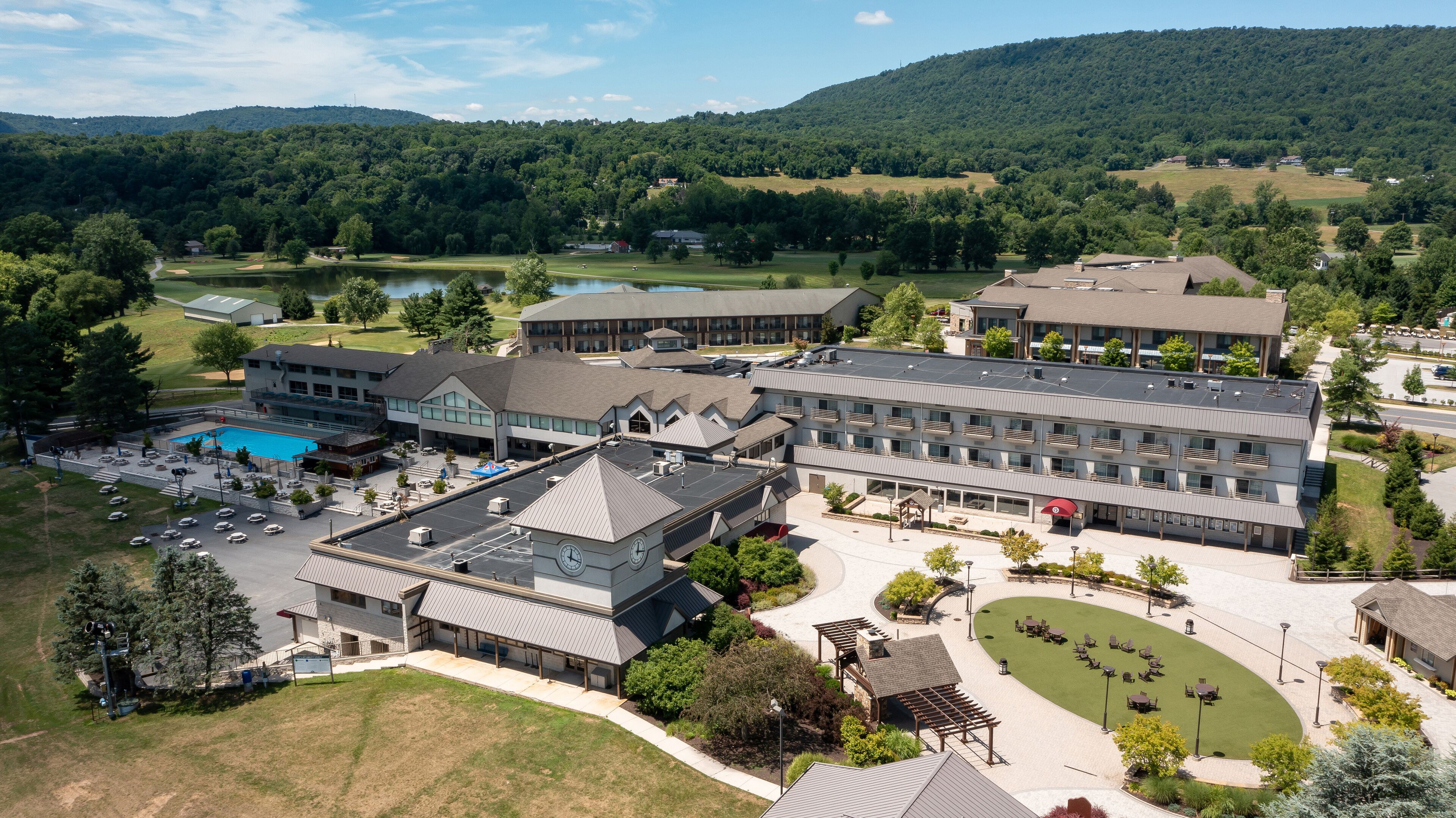 An aerial view of a hotel with multiple buildings, a swimming pool, and a golf course in the background.