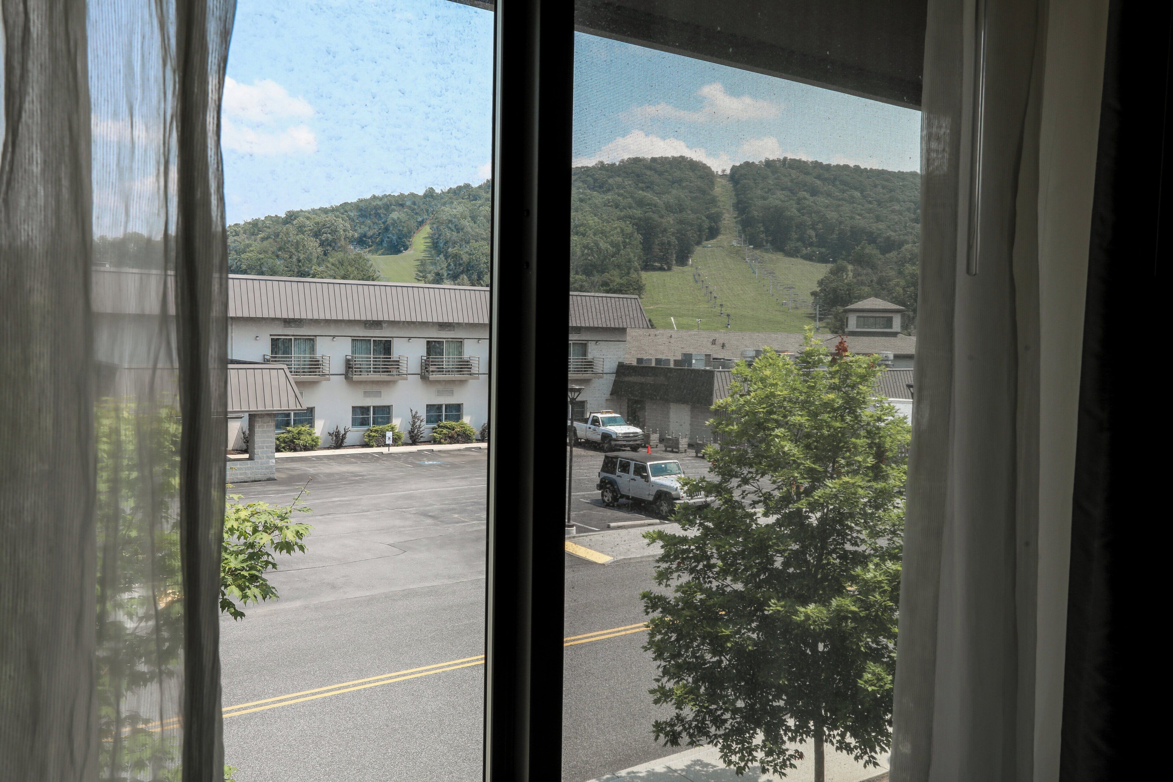 Vista a través de una ventana que muestra un estacionamiento, edificios y una colina al fondo.