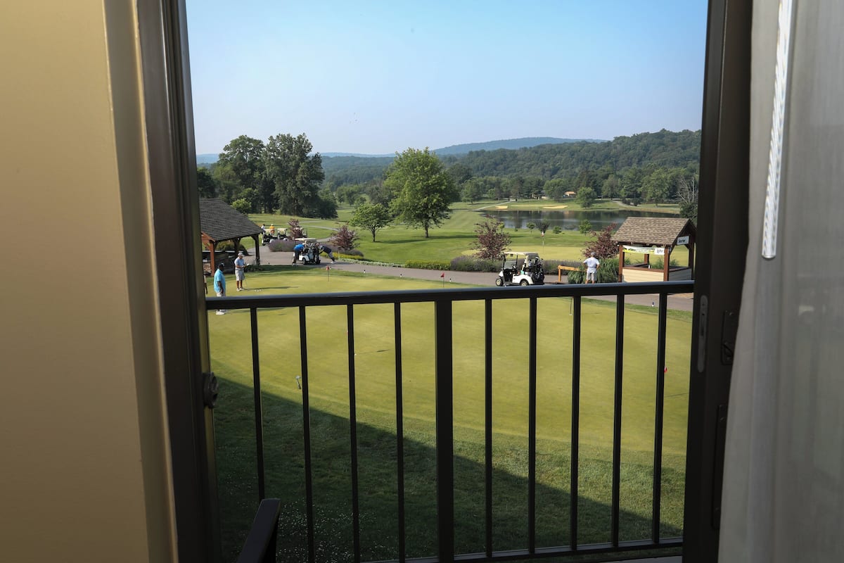 A view from a balcony overlooking a golf course with a pond, trees, and distant hills.