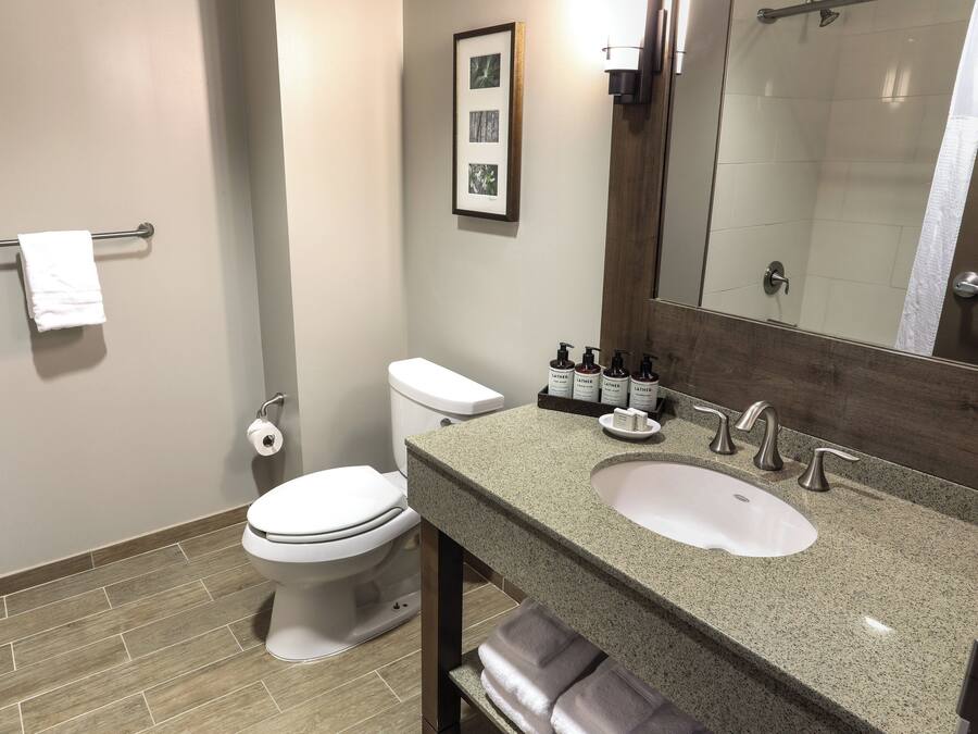 A bathroom with a toilet, sink, and mirror. There are towels on the counter and a picture on the wall.
