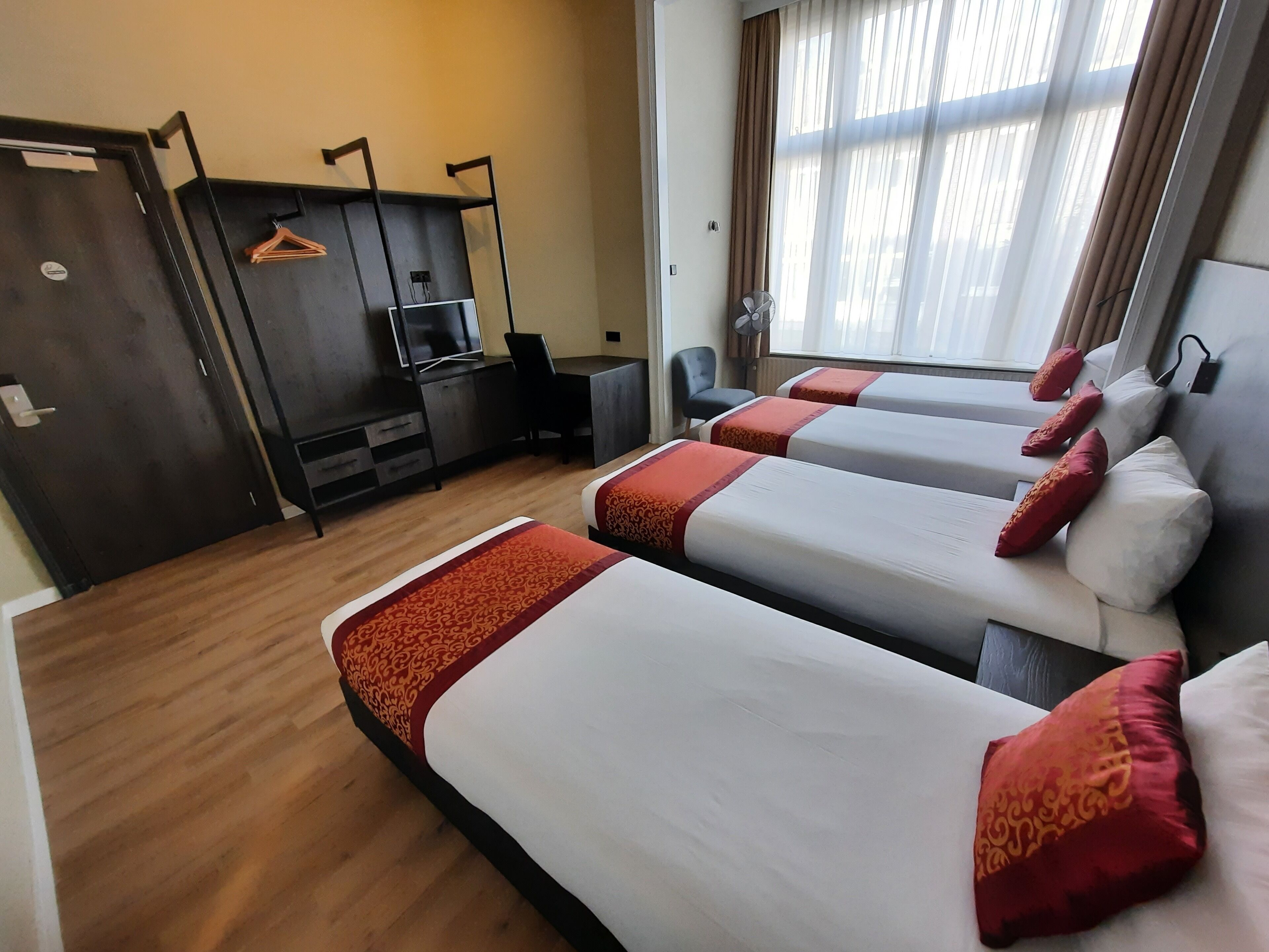 A hotel room with three single beds, a desk, a chair, a TV, and a wardrobe.