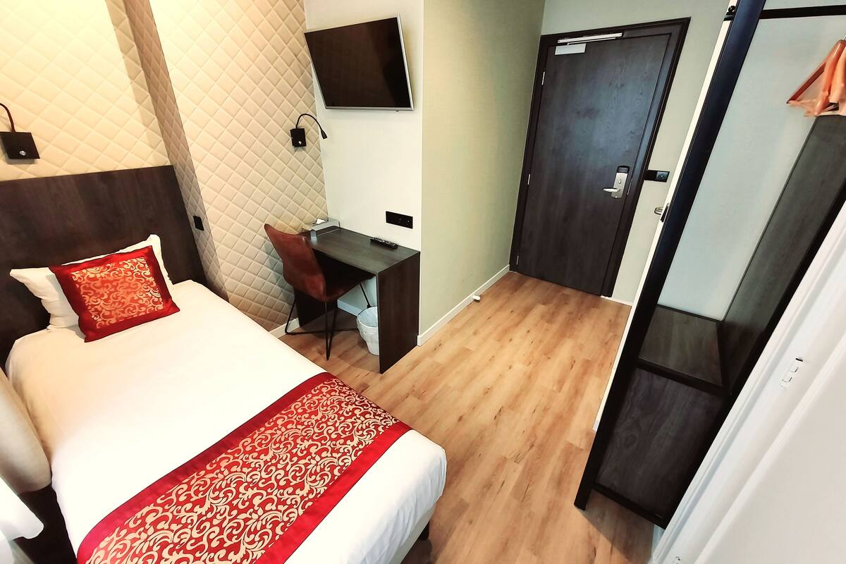 A hotel room with a bed, a desk, a chair, a TV mounted on the wall, and a door.