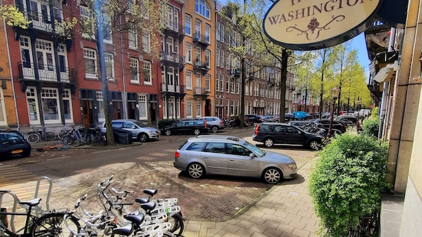 Une vue de rue avec une enseigne indiquant l’hôtel Washington, mettant en valeur une architecture traditionnelle et des voitures garées.