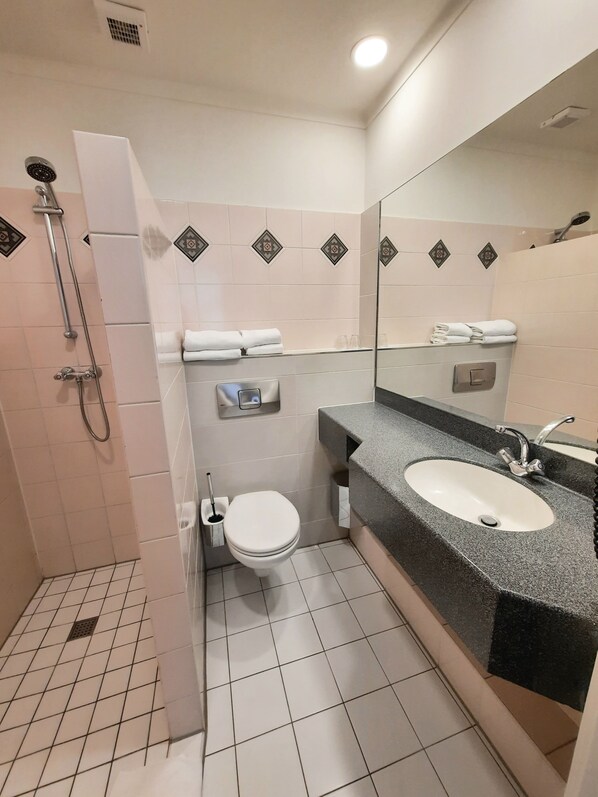 A bathroom with a shower, toilet, sink, and a mirror.