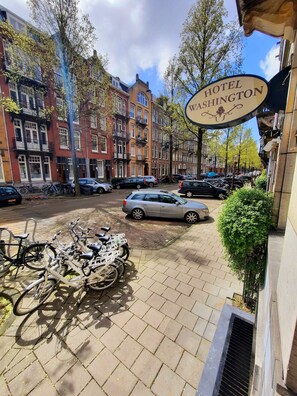 Vista da rua com bicicletas estacionadas, carros e uma placa para o Hotel Washington.