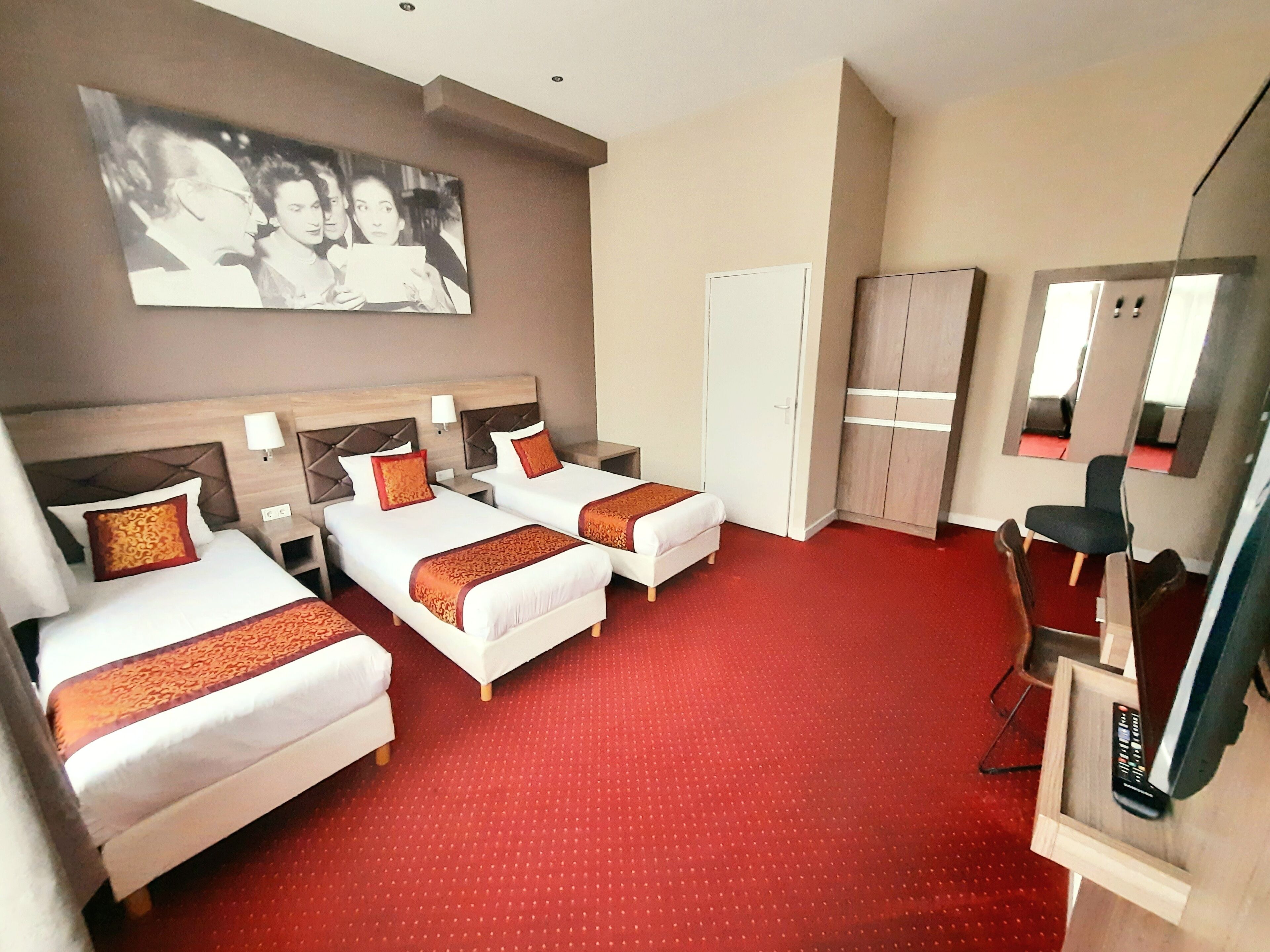 A hotel room with two beds, a wardrobe, a mirror, and a television.
