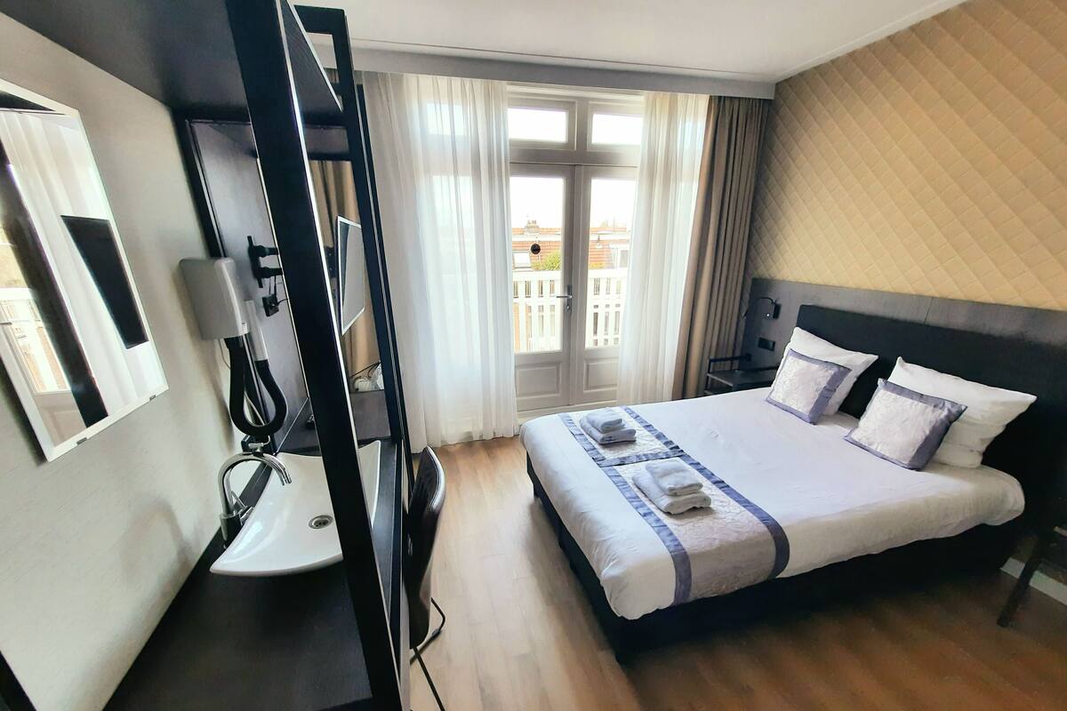 A hotel room with a bed, a desk with a chair, a television, and a window with curtains.
