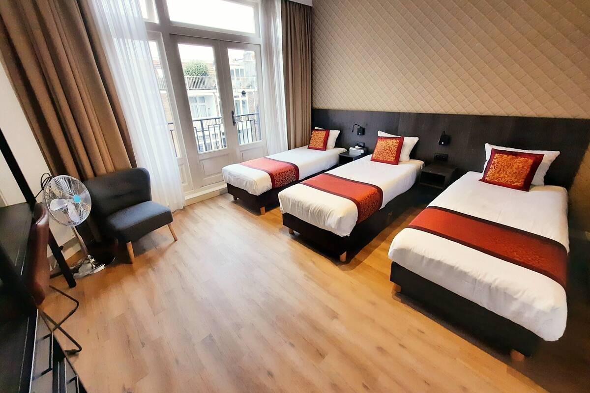 A hotel room with three beds, a desk, a chair, and a window with curtains.