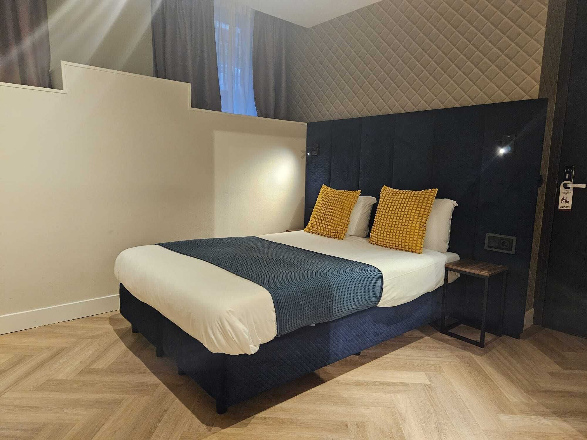 Ein modernes Hotelzimmer mit einem großen Bett, einem dunklen Kopfteil und einem kleinen Nachttisch.