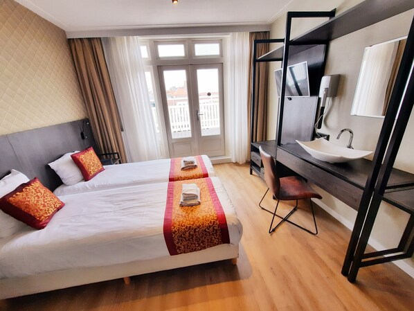Une chambre d’hôtel avec deux lits, un bureau doté d’un lavabo et une grande fenêtre avec des rideaux.