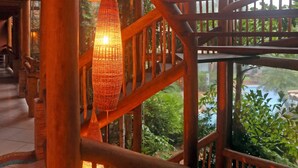 Un escalier en bois, doté d’une rampe, mène à un espace extérieur offrant une vue sur la verdure et une étendue d’eau.