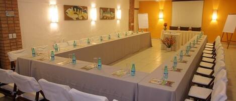 Ein Konferenzraum mit einem langen Tisch, Stühlen und einer Projektionsleinwand.