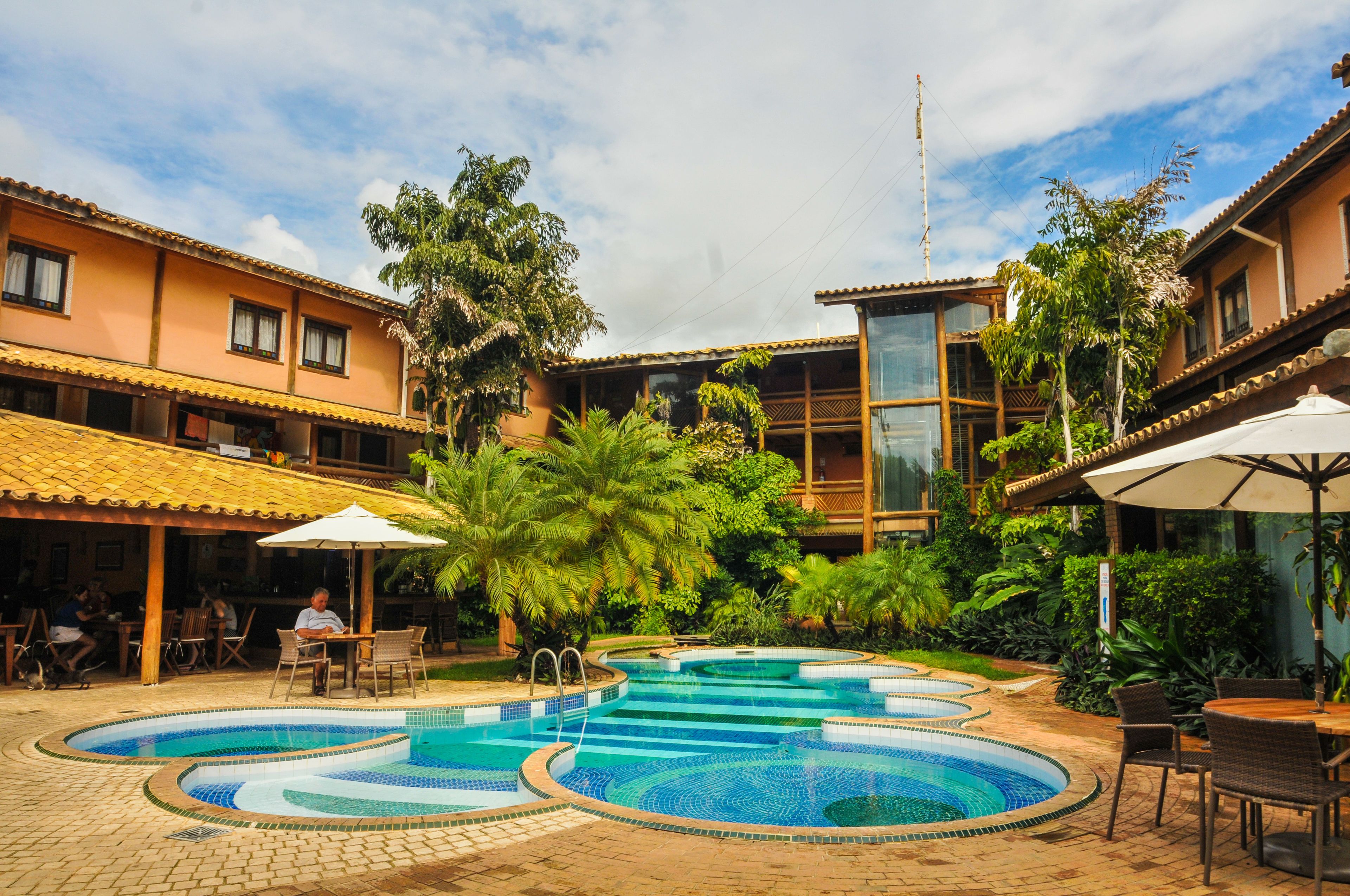 A pool area with multiple swimming pools, outdoor seating, and lush greenery.
