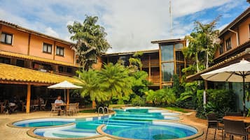 Un área de piscina con varias piscinas, mobiliario exterior y abundante vegetación.