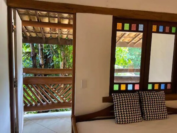 A room with a bed, a wooden headboard, a window with colorful notes, and a view of greenery outside.
