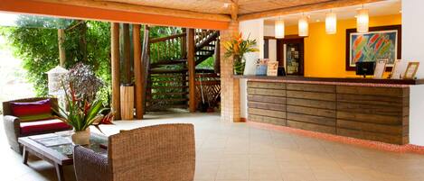 Un área de recepción con un mostrador de madera, mobiliario de mimbre y vistas al exterior.