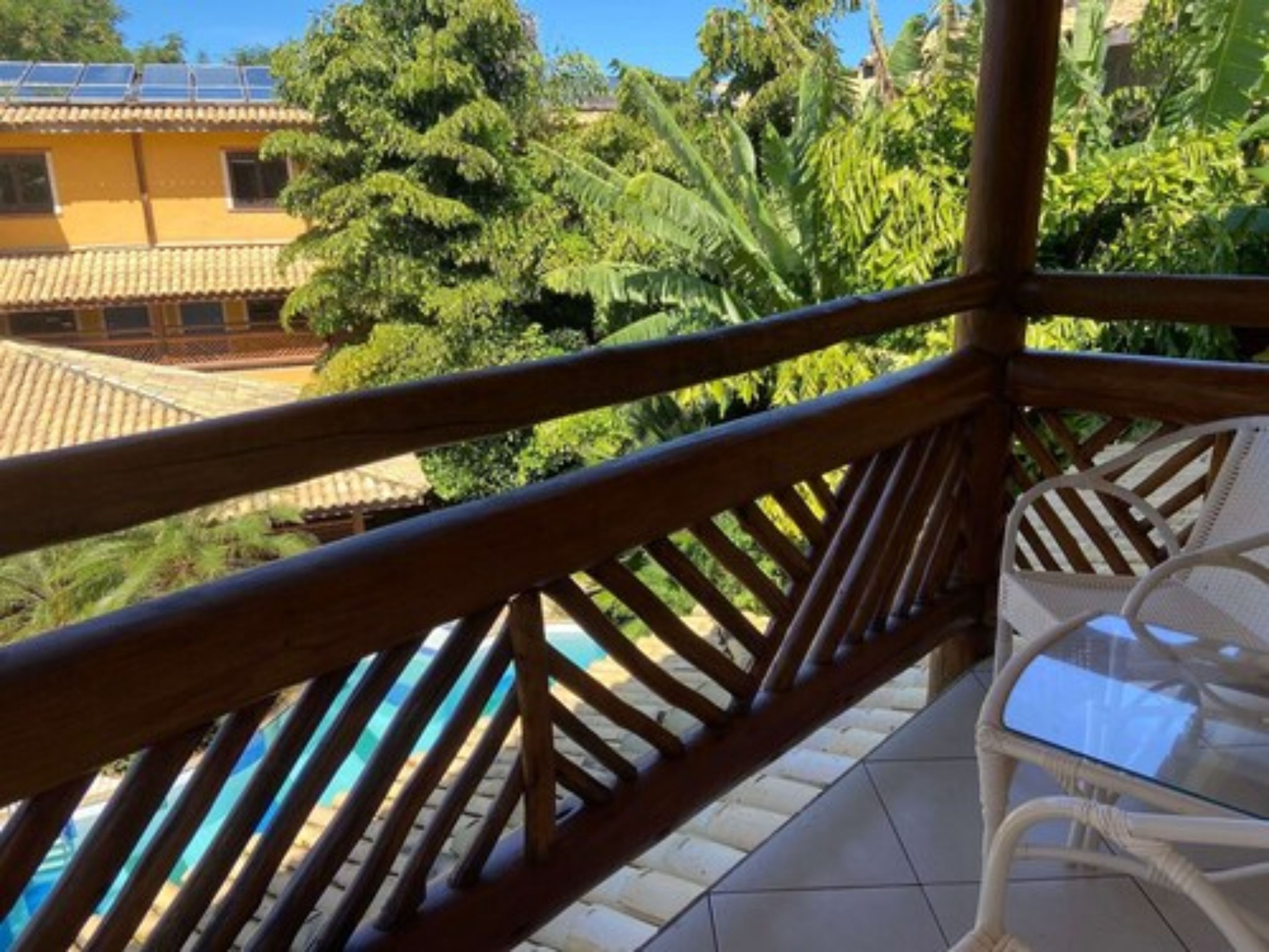 A balcony with a view of a house, a pool, and lush greenery.