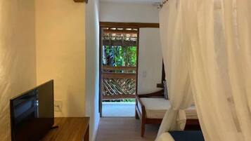 Un dormitorio con una cama, un televisor sobre una mesa de madera y vistas a un jardín a través de una celosía de madera.